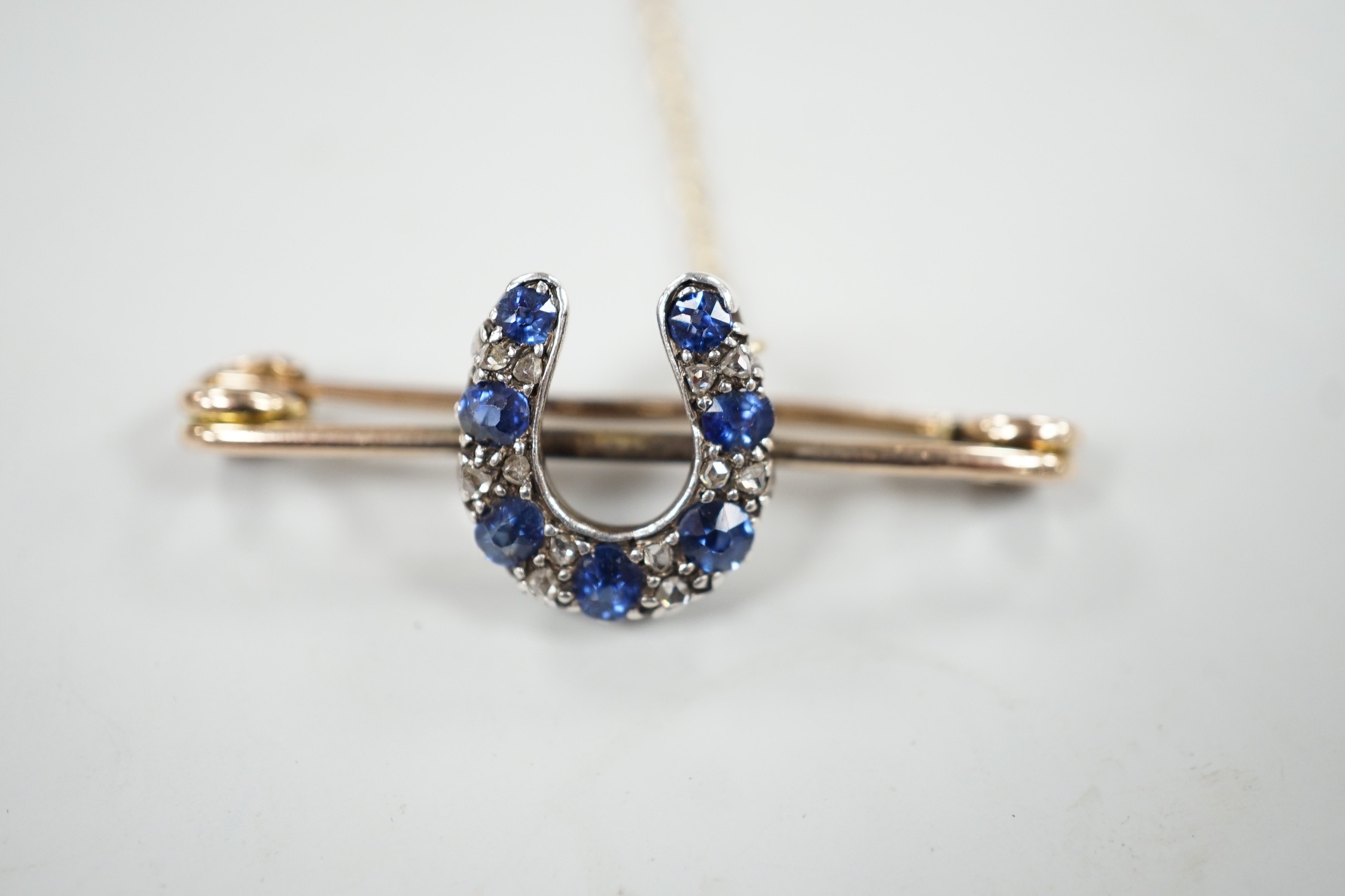 A late Victorian yellow metal. sapphire and diamond cluster set horseshoe bar brooch, 42mm, gross weight 5.3 grams.